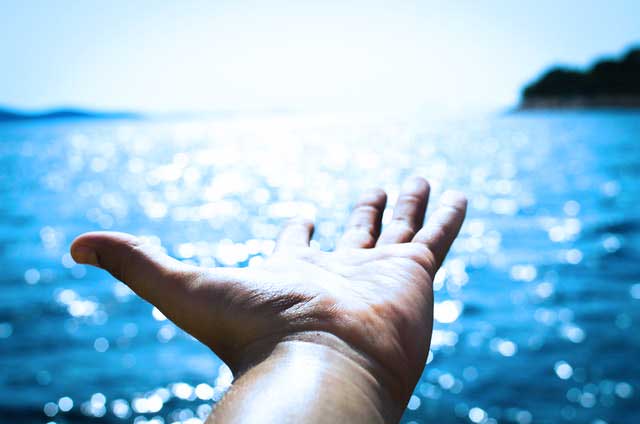 Hand with the palm up in front of blue water