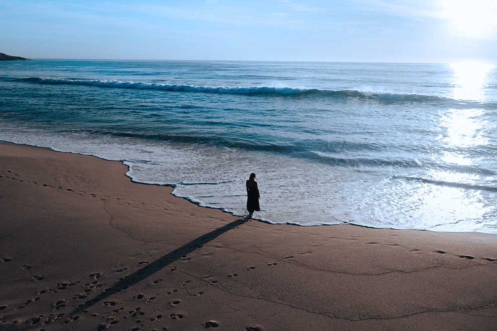 Woman standing in front of blue ocean with sun in sky